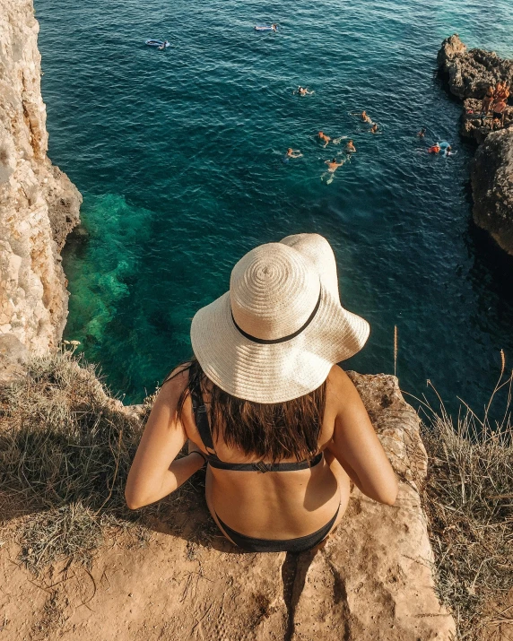 a person in a hat looking over water from a cliff