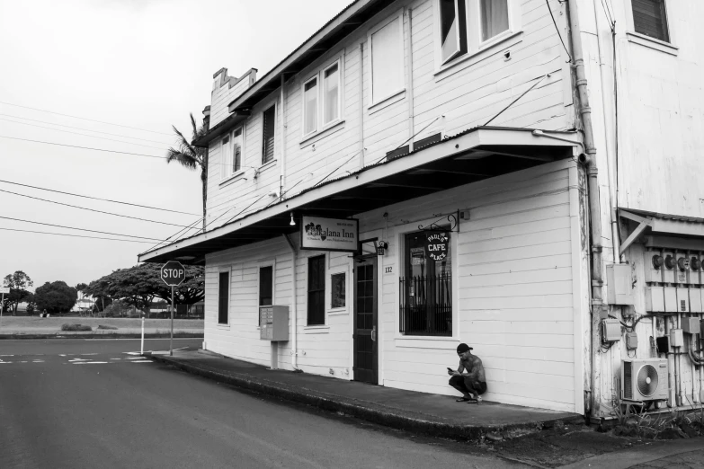 black and white pograph of man sitting outside the front door of an old rundown bar