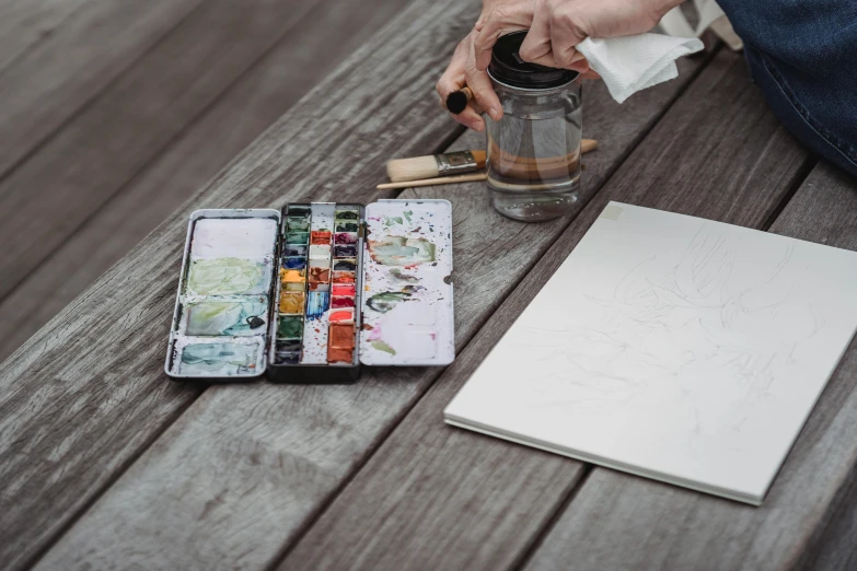 the person is painting with watercolors on the table