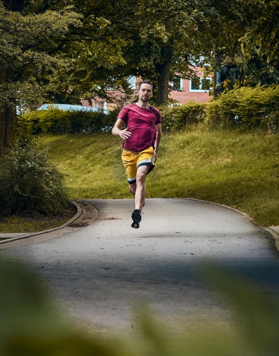 man in maroon shirt running on roadway through wooded area