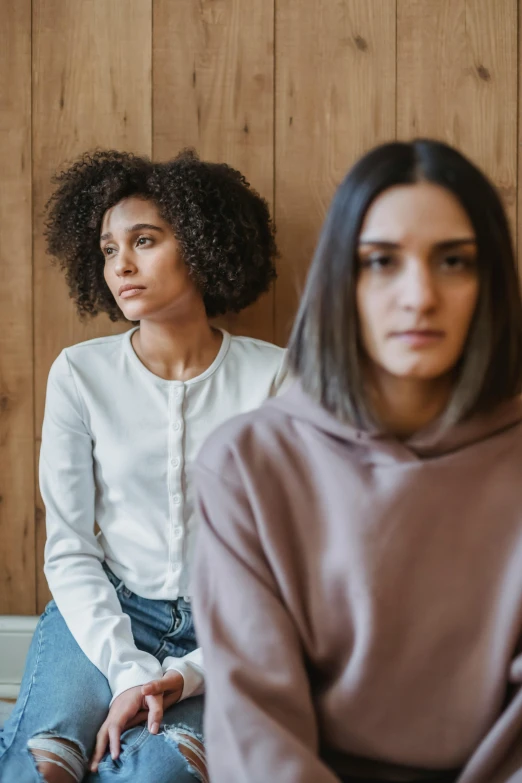 two women sitting on a chair with their hands in their pockets