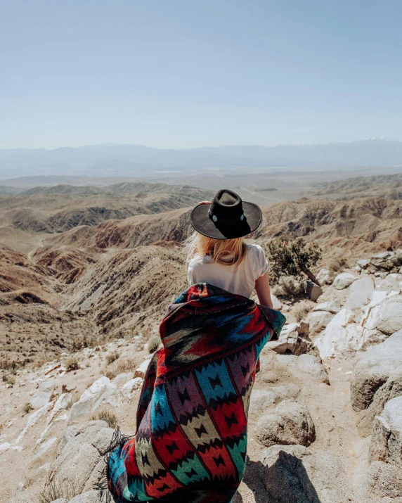 the lady in the black hat is sitting on the rock