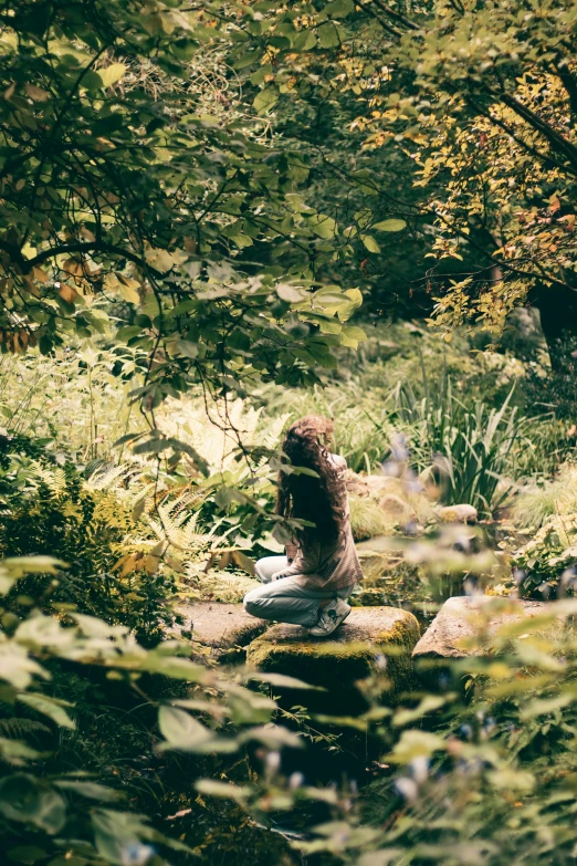 a woman sitting on rocks in a forest with a white towel around her neck