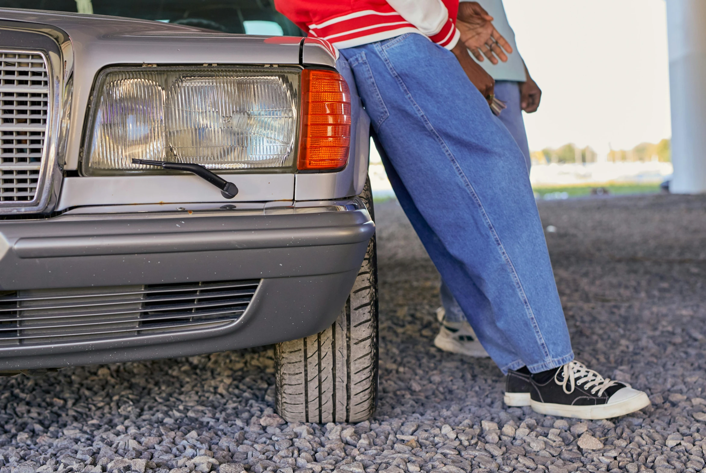 a man in jeans standing on the front of a parked car