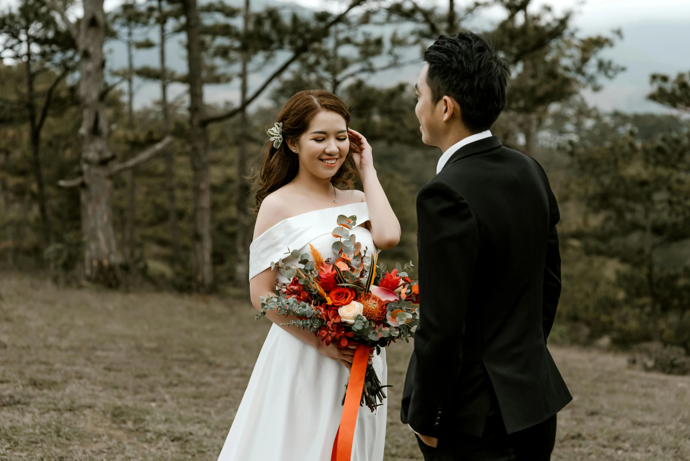 a bride with a floral bouquet stands next to the groom in the woods