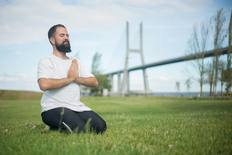 a man sits in the grass, with his arms crossed and his eyes closed