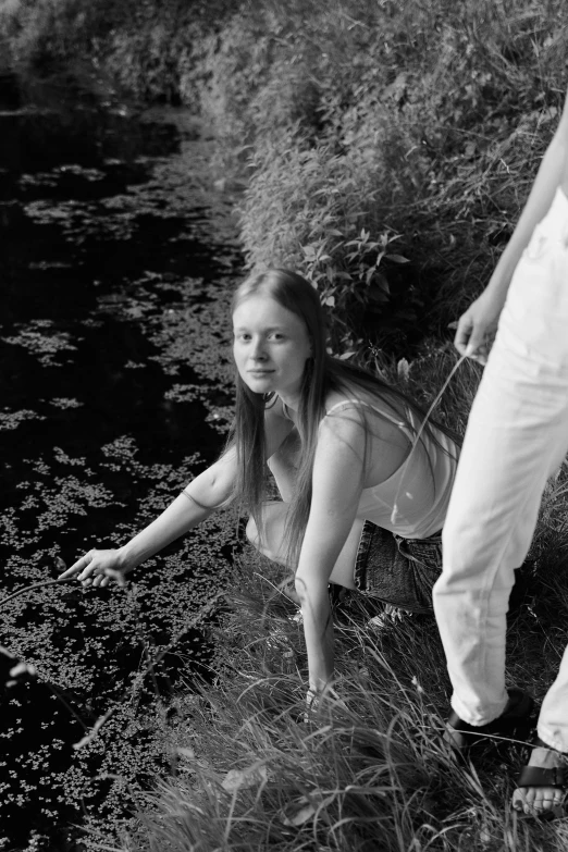 black and white po of a girl in the grass near a river