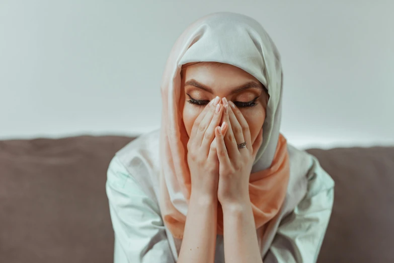 woman in hijab covering face with hands