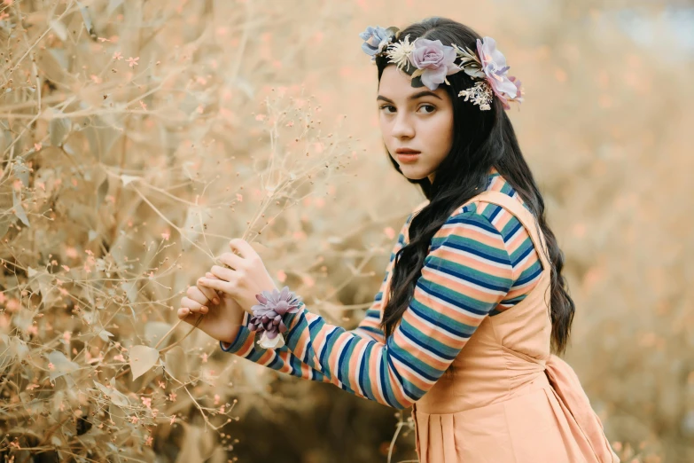 a woman wearing a pink flower crown stands in a field