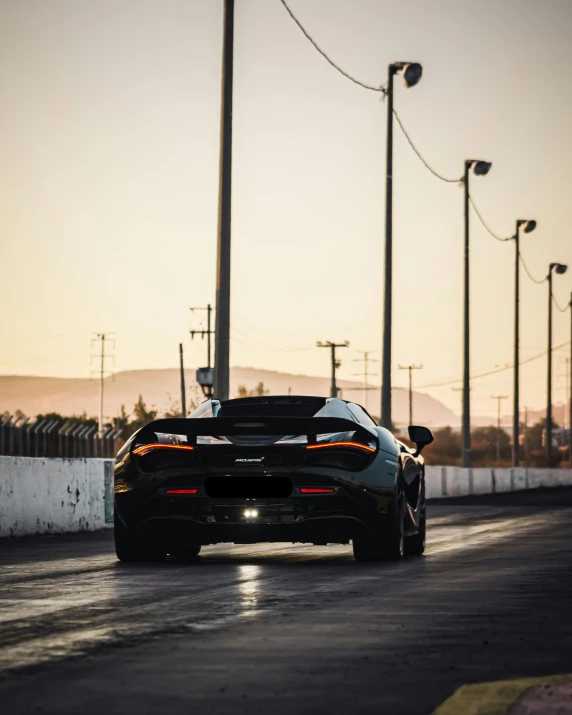 a sports car driving down a wet track at sunset