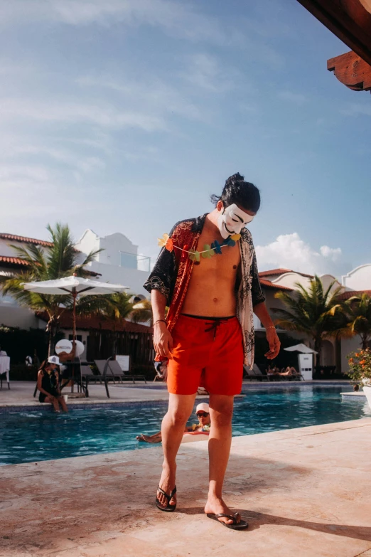 a guy in orange swim trunks standing near a swimming pool