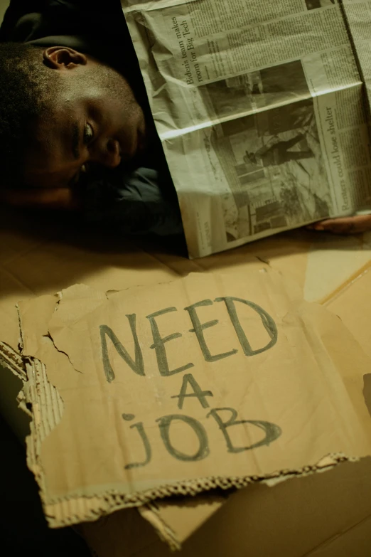 man lays on cardboard next to some newspaper