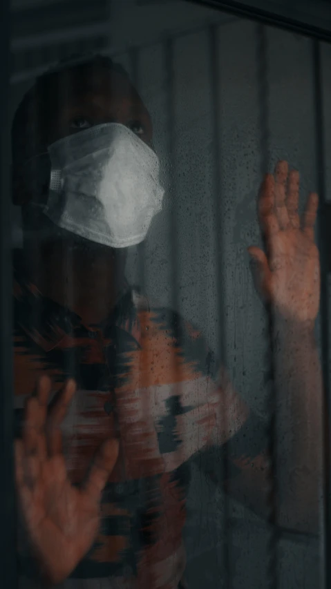 a man looking through a window with his hand and face covering