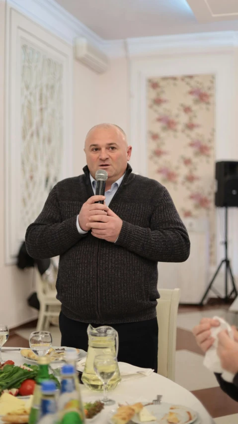 the man is speaking into the microphone near a table with food