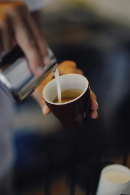 a coffee cup with coffee being poured out is held by two hands