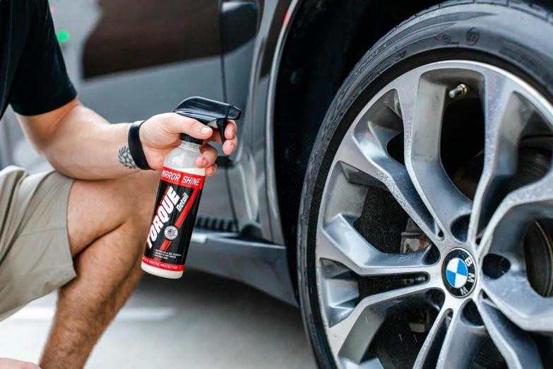 man sitting down putting the last bit of tire cleaner on a car