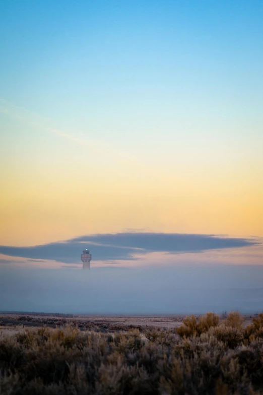 a distant po of a lone tower in the distance with a foggy field to the side