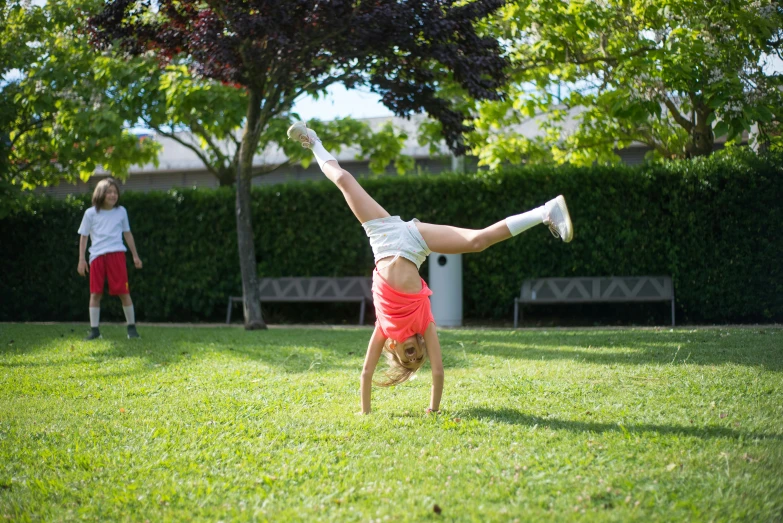 a  performs a handstand on the grass in front of two other s