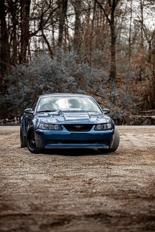 the front of the blue car is parked in a field with the trees behind it