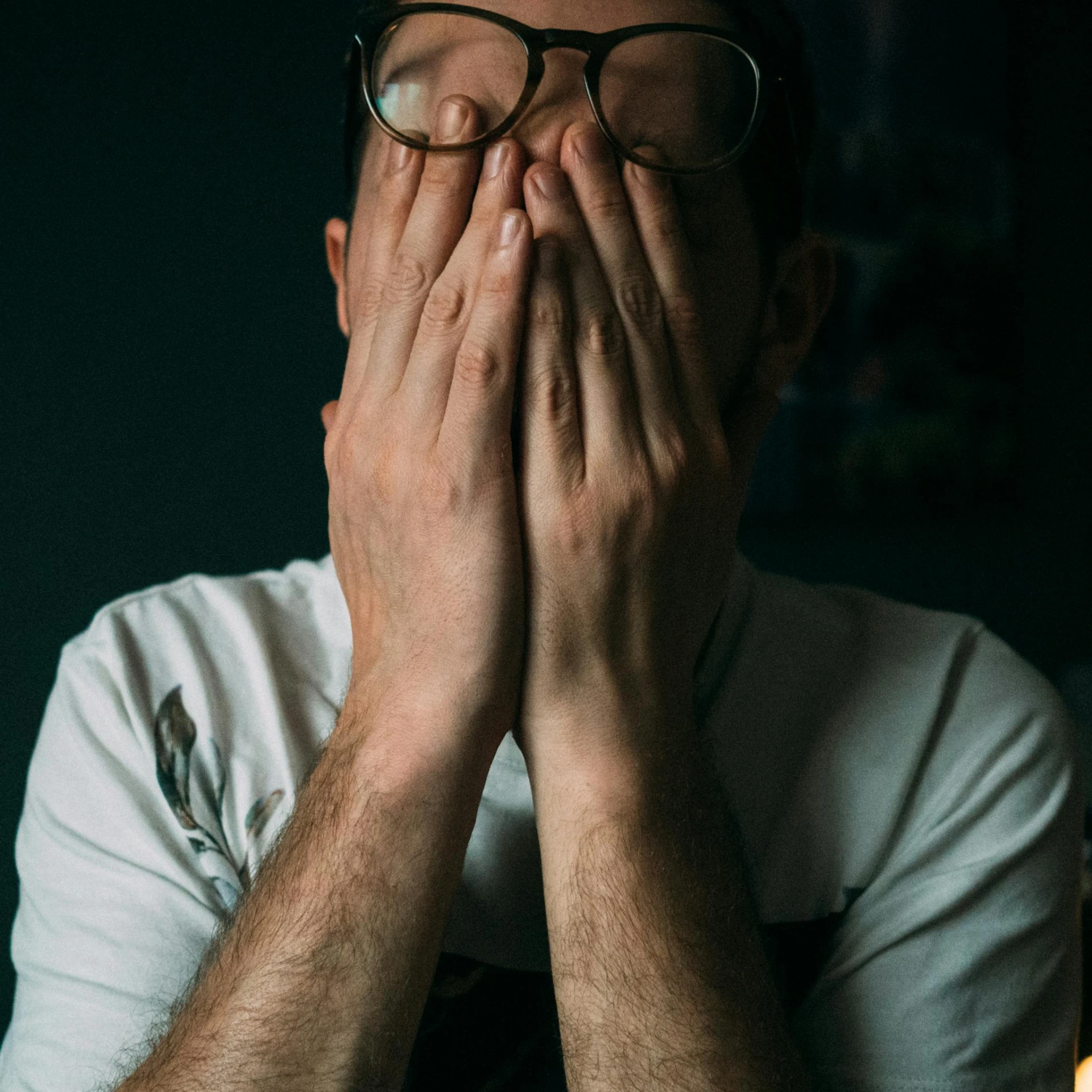 man covering his face with hands while sitting at the table