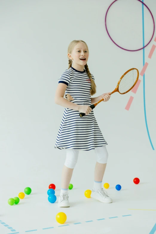 a girl standing on a floor with balls and a racket