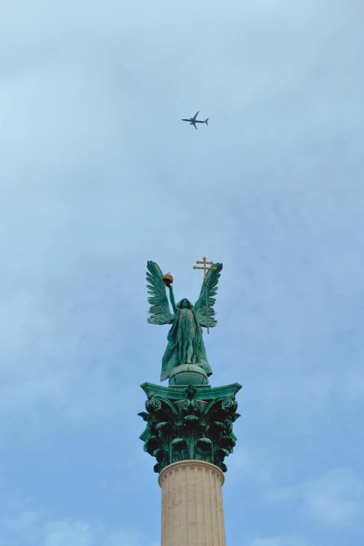 a jet flying over a statue with the sky behind it