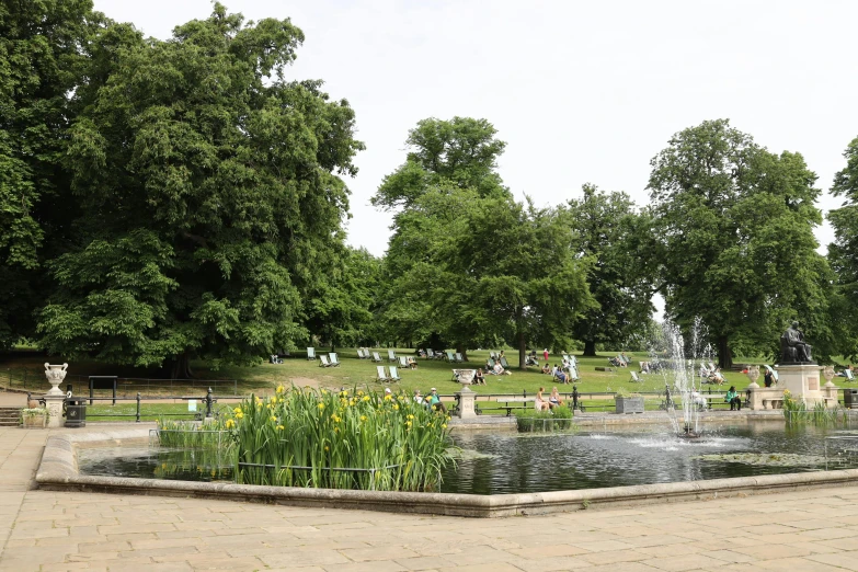 the park with a fountain and many people sitting at it