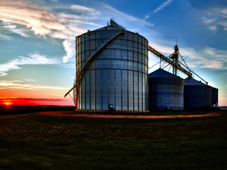 the sun rises above two silos on a farm