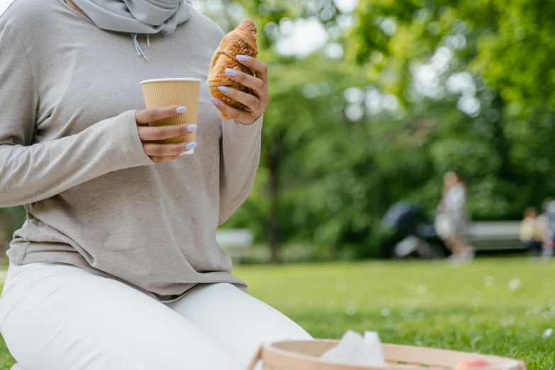 a woman in a scarf is sitting on the grass while eating a pastry