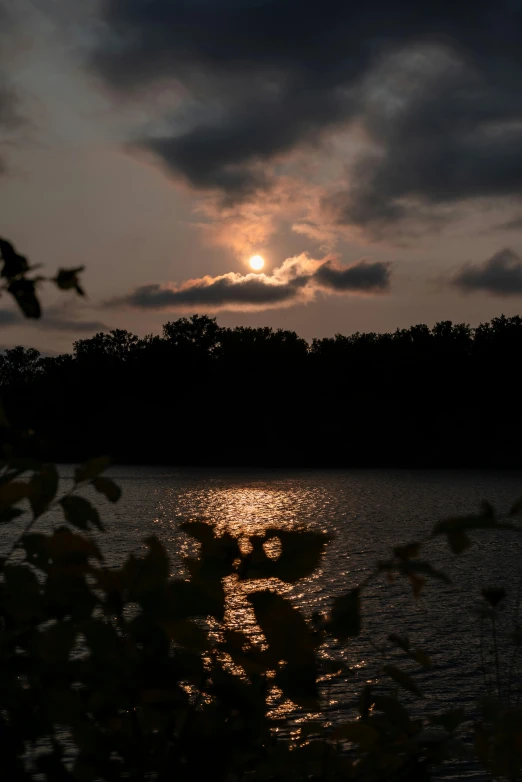 the setting sun over a lake surrounded by trees