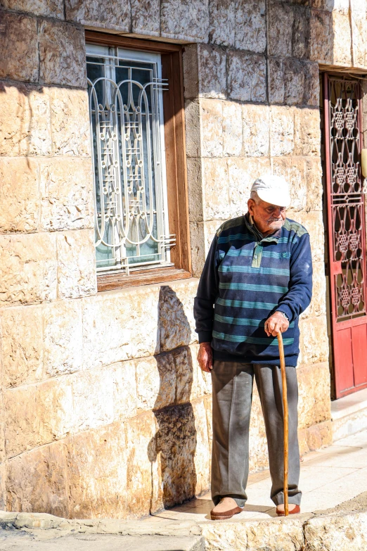 an elderly gentleman stands near a water fountain and stone building