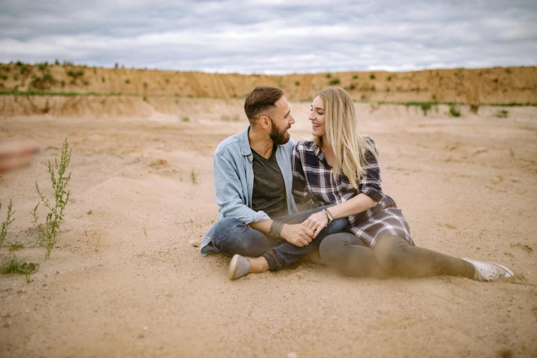 two people sitting in the sand looking into each others eyes