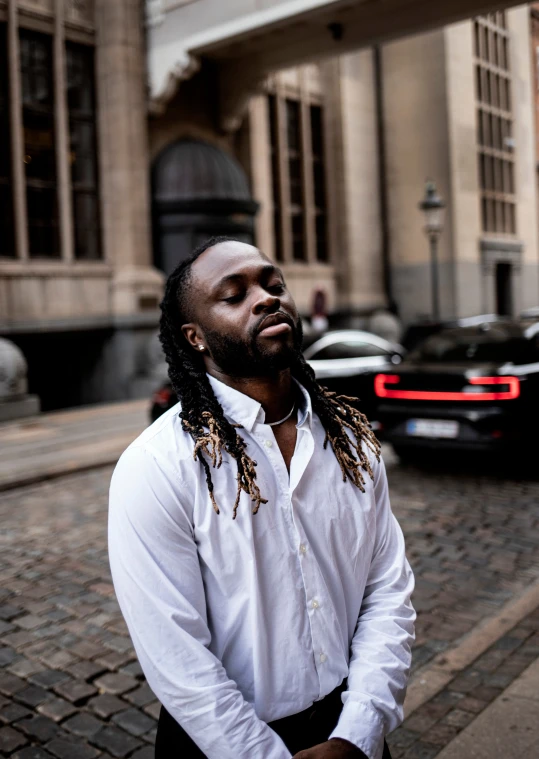 a black man with long dreadlocks on standing next to a building