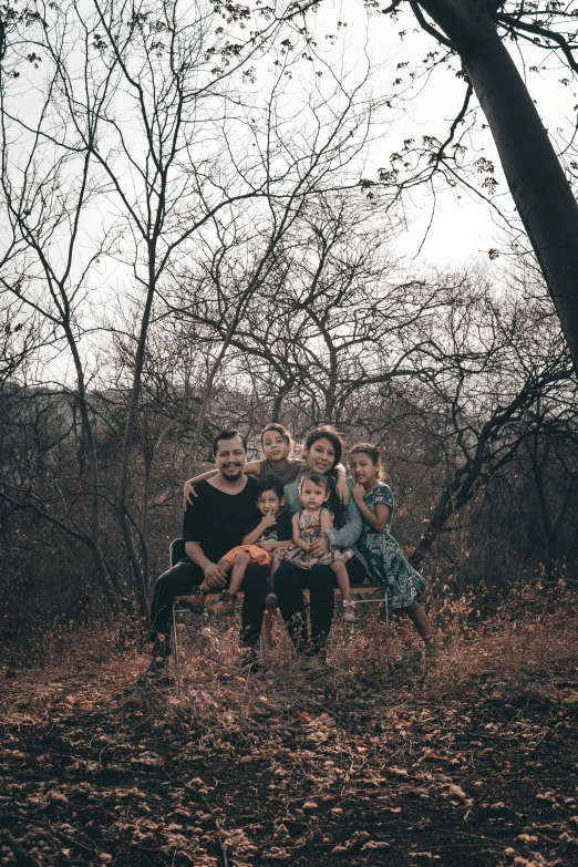 family poses on a bench by some trees