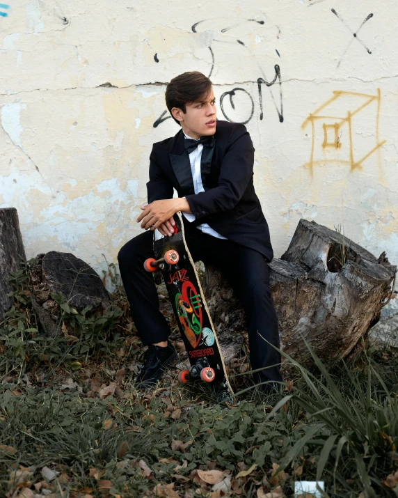 a man in a suit sitting on some rocks holding a skateboard