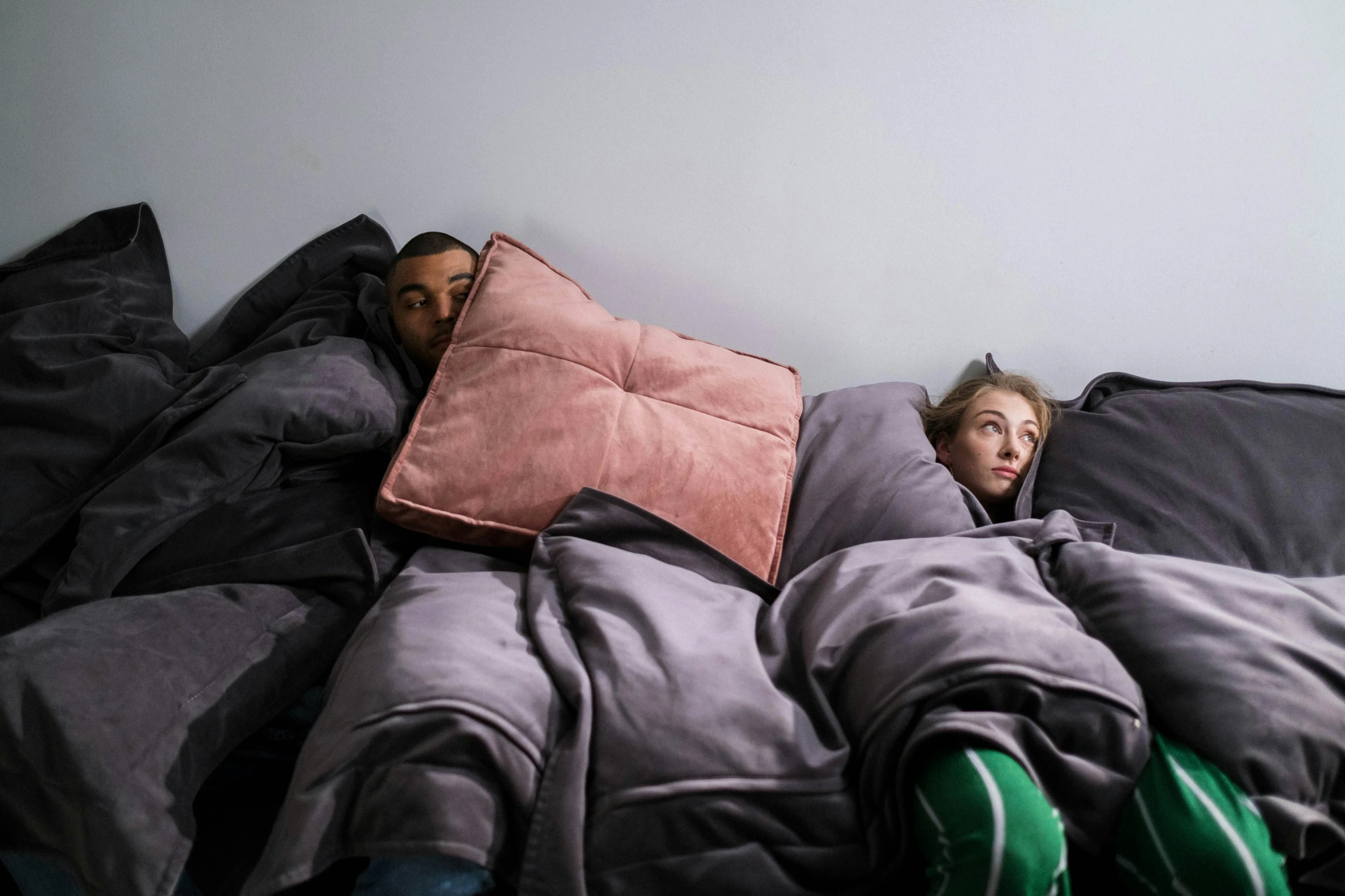 two people laying in bed covered by covers with pillows