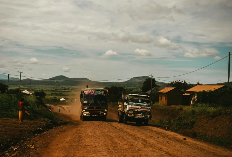 two trucks moving down a dirt road through an open area