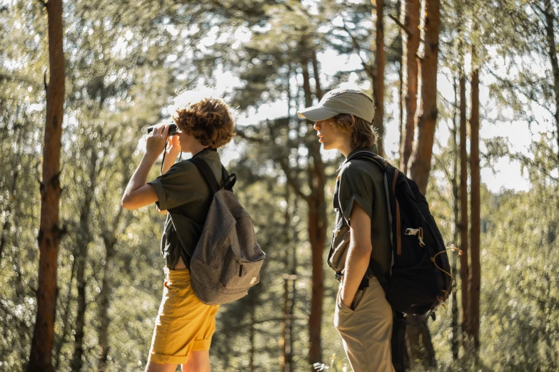 two people walking through the woods while one is using his cellphone