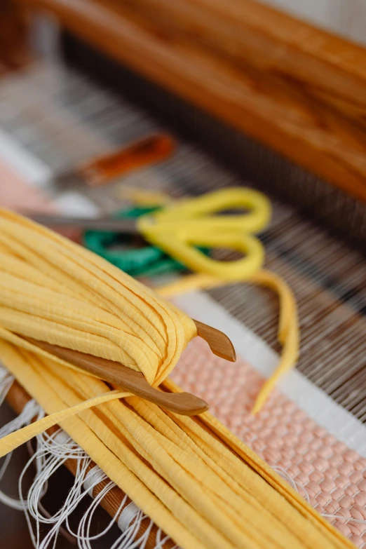 a pair of yellow scissors next to a weaving needle