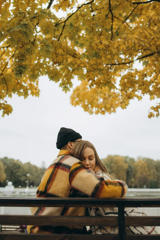 a man and woman sitting on a park bench under an autumn tree