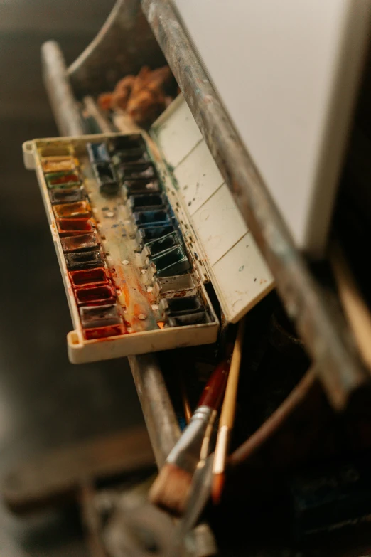 a brush, paint, and watercolor palette sit together in an easel