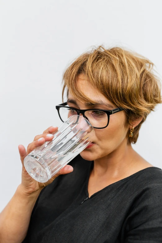 a woman in glasses is drinking from a glass