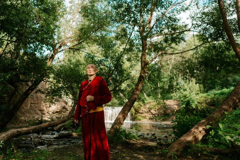 a man in a red robes stands by trees