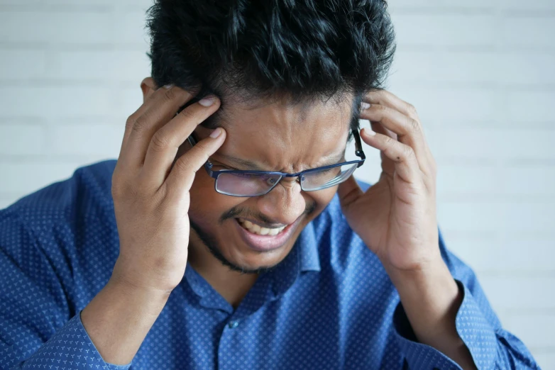 a man in glasses has his hands to his head and is upset with soing