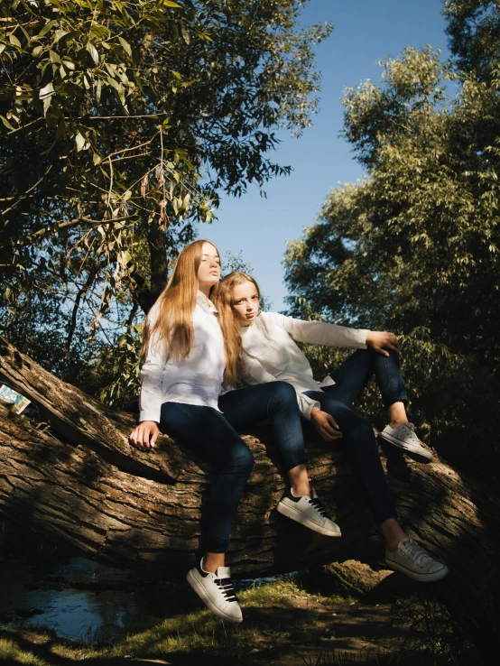 two women posing on a tree limb in front of some water