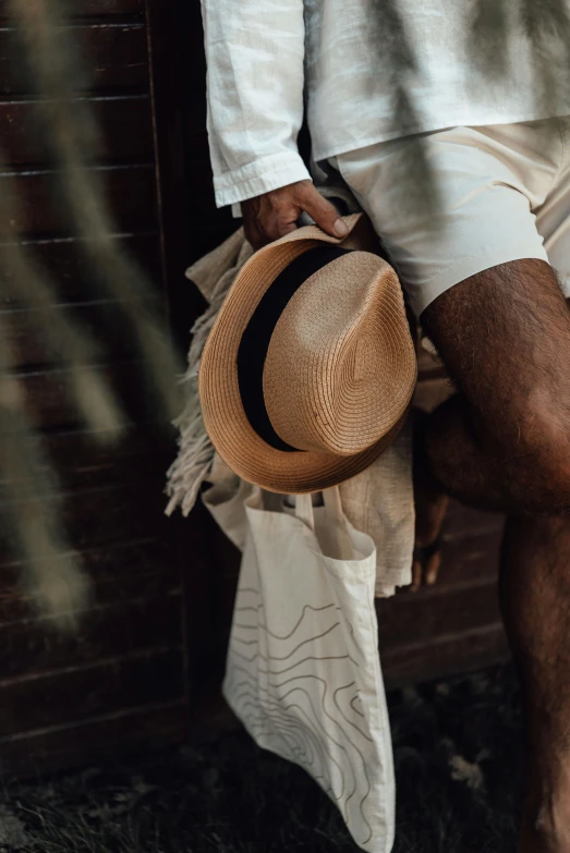 a man holding a tan hat in one hand and standing next to a wall