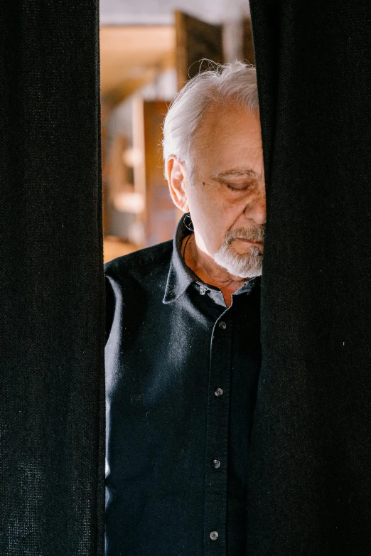 man staring out from behind a curtain looking at soing