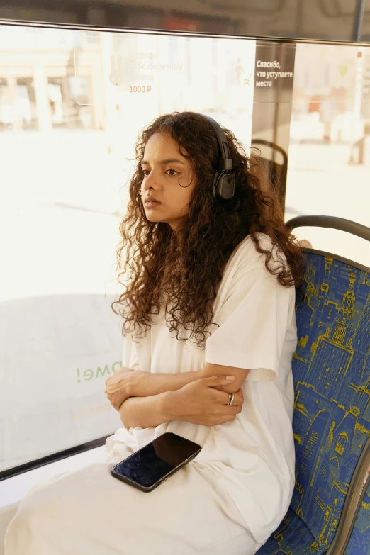 a woman in headphones sits on a bus seat and looks into the distance