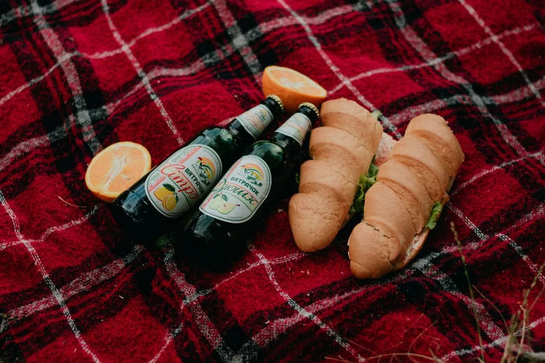 beer, bagels and an orange are sitting on a blanket