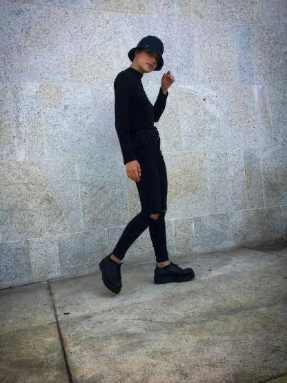 young man in all black walking against a wall